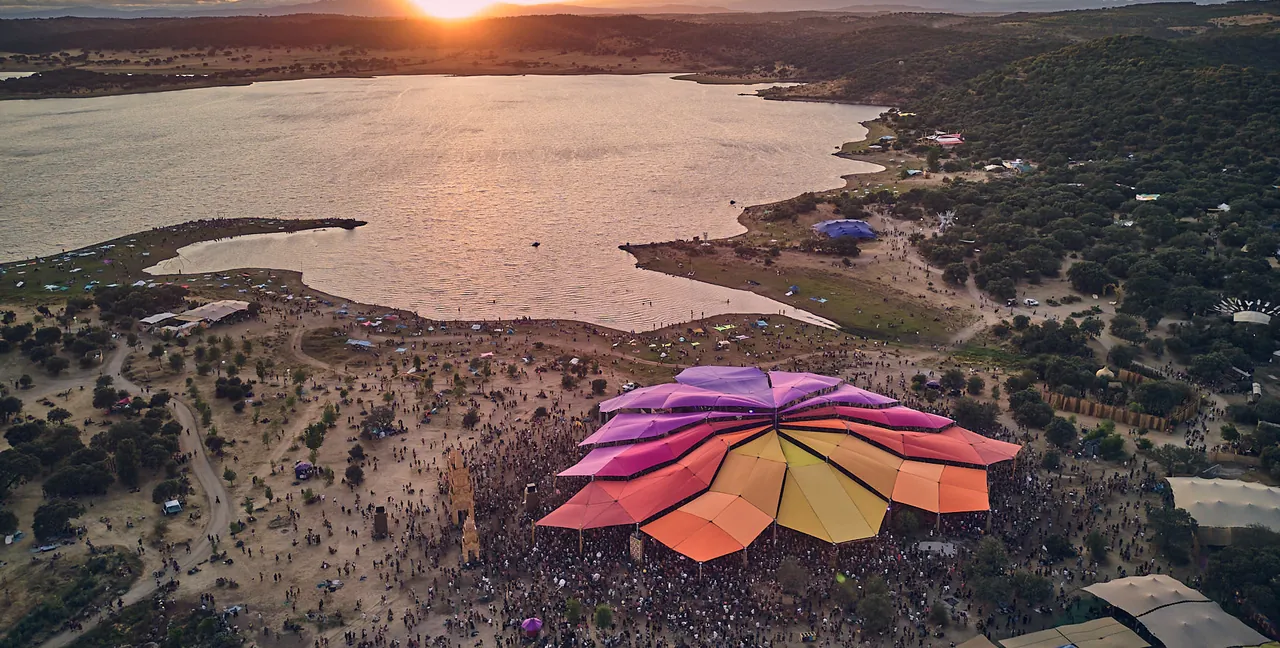 Vue aérienne de Boomland au coucher du soleil : le lac de barrage Marechal Carmona et, au premier plan, une grande scène en forme de fleur.