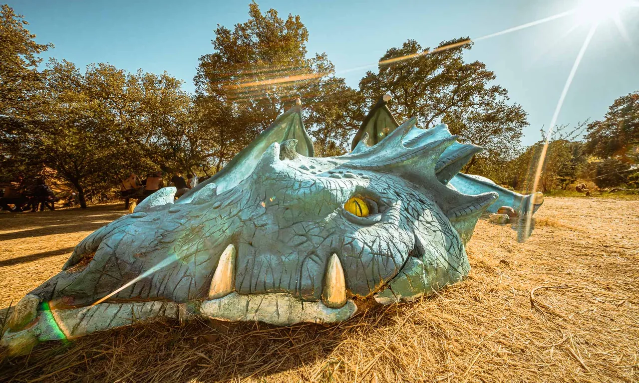 Tête de dragon sculptée posée dans l'herbe sèche, l'une des installations disséminées sur le site.