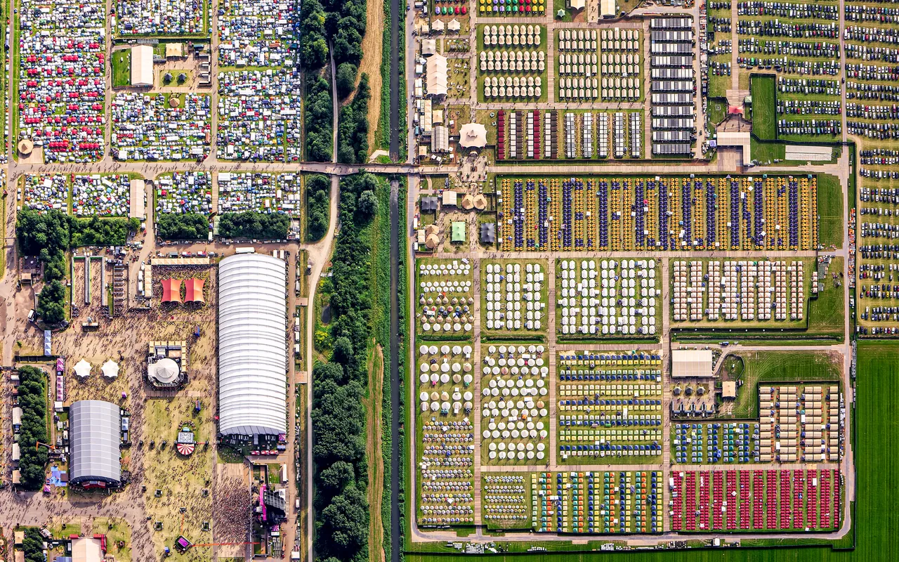 Vue aérienne de Biddinghuizen pendant Defqon.1 2024 : à gauche le site du festival et ses grandes halles, à droite les Camping Grounds quadrillés.