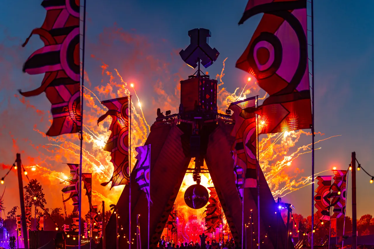 Un totem du site et ses bannières, feu d'artifice en arrière-plan, le soir de The Gathering, jeudi 25 juin 2026, seule soirée de l'édition à avoir eu lieu.