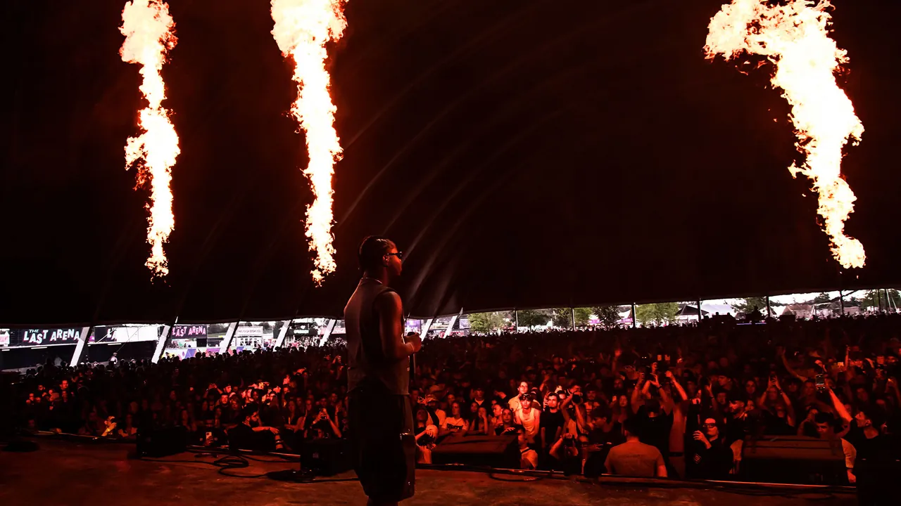 Boombox at night: flame columns above the stage, facing a packed tent.