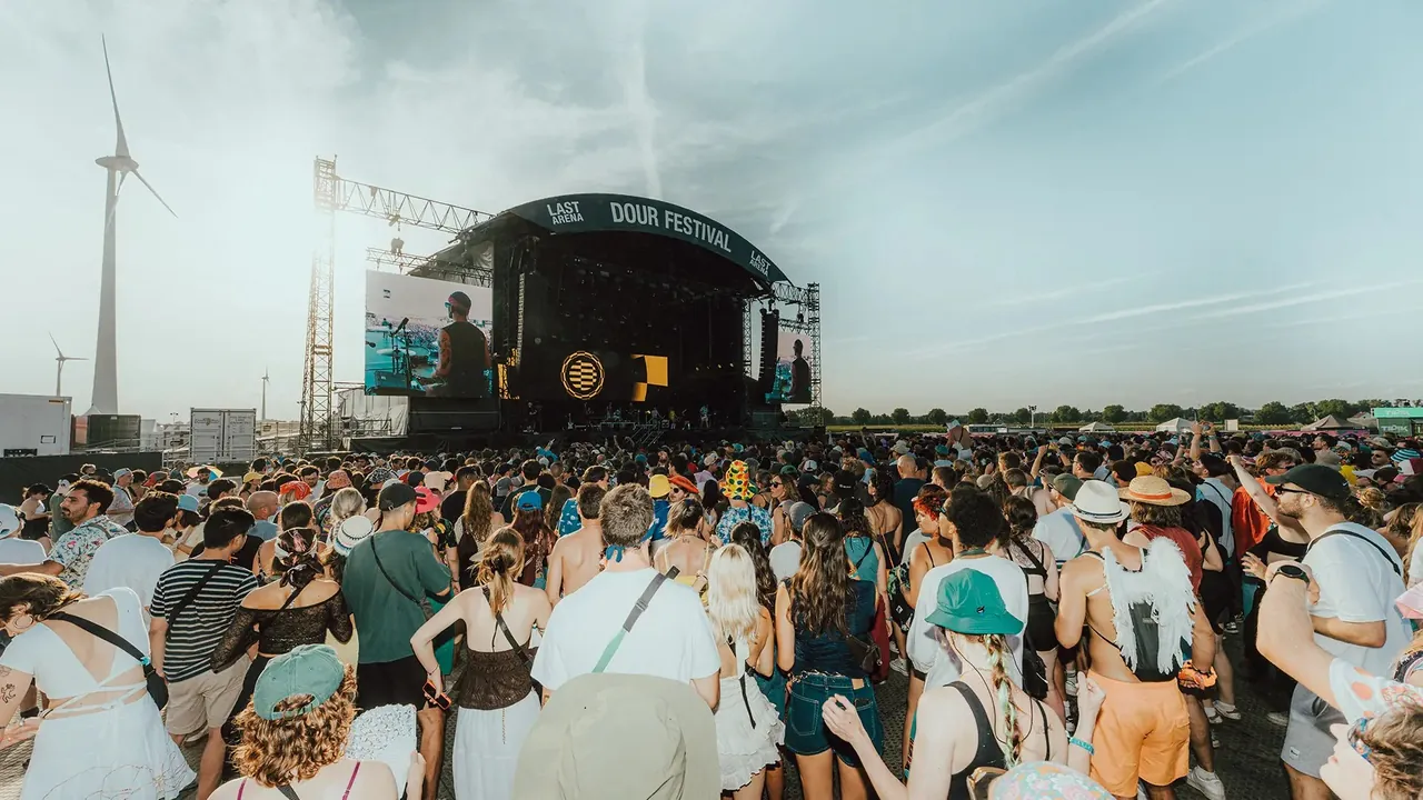 Afternoon at The Last Arena, the crowd facing the main stage next to a wind turbine.