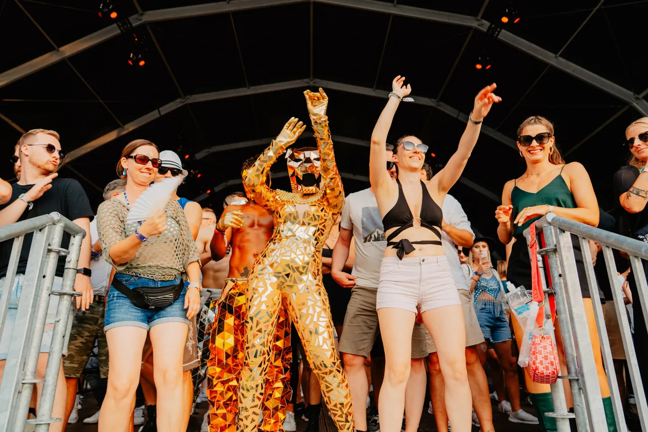 Festivaliers sous un chapiteau, dont un danseur en combinaison à miroirs dorés, le 5 juillet 2025.