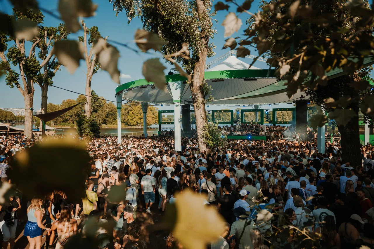 La foule entre les arbres du Sloterpark devant une scène au bord du lac, le dimanche 10 août 2025.