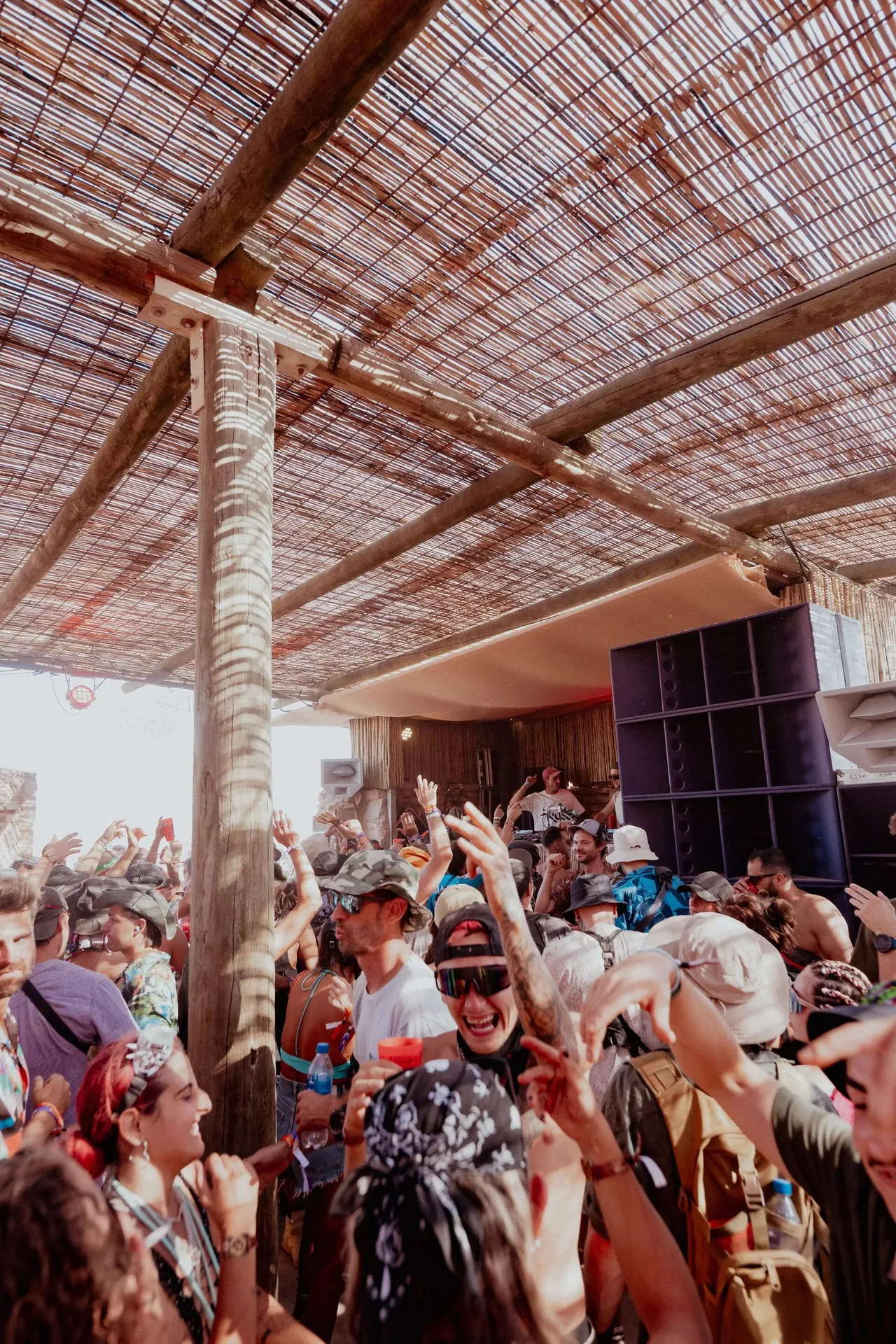 A small stage sheltered under reed matting, in front of a wall of handmade speakers.