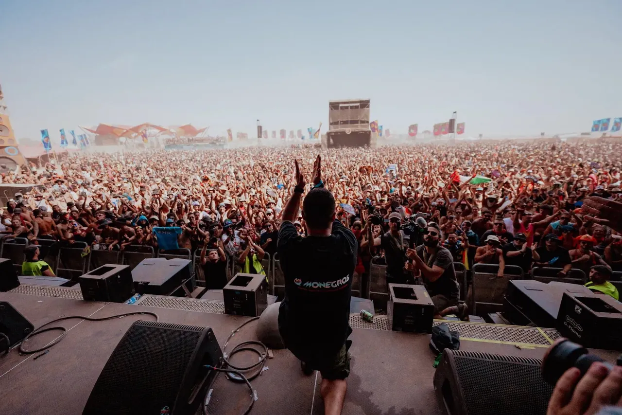 A DJ greeting a huge daytime crowd, with the desert on the horizon.