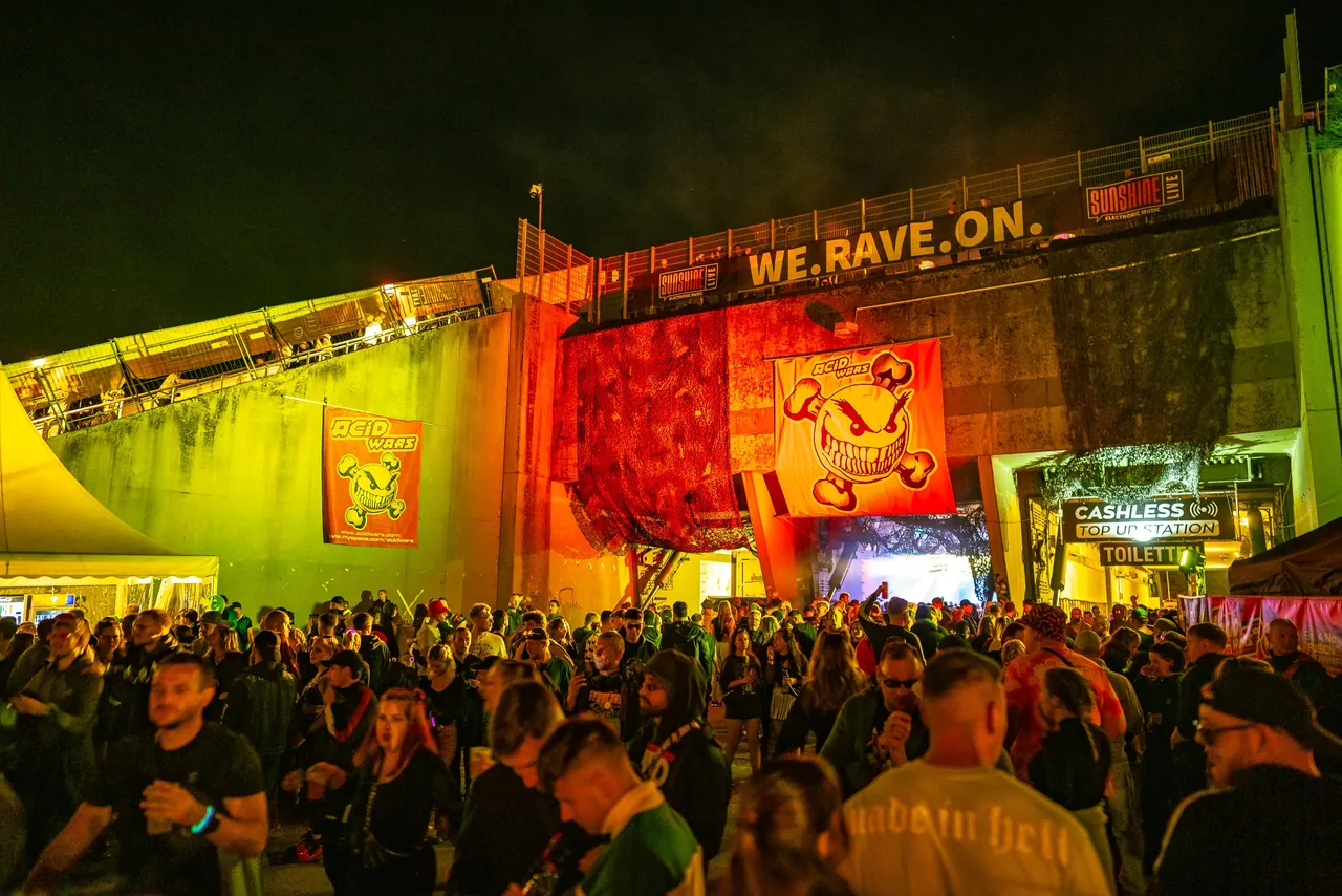 Devant un bunker de la Pydna en 2023 : l'entrée du floor Acid Wars, à l'intérieur du béton, sous la bannière « We.Rave.On. ».