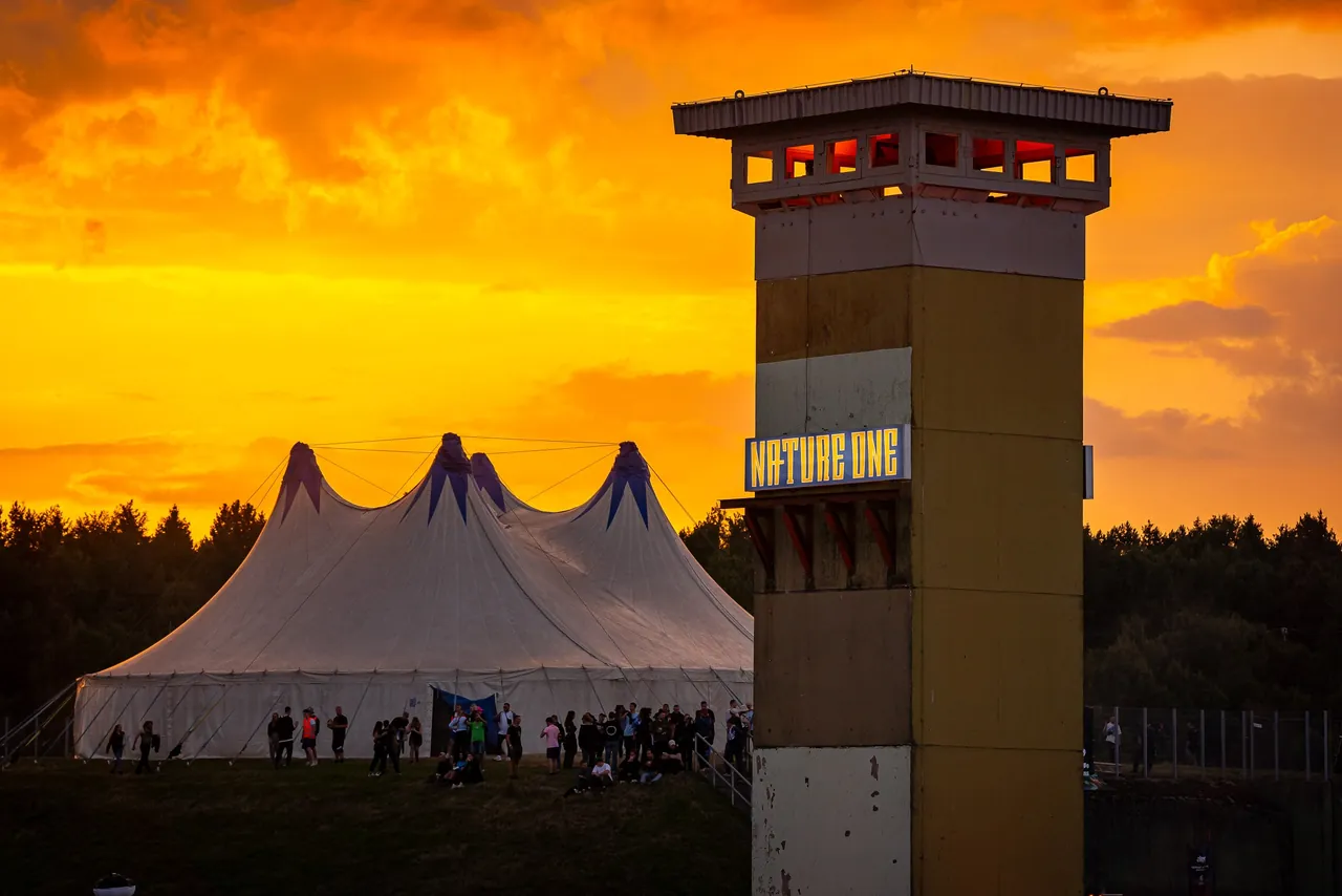 La tour aux couleurs de Nature One et un chapiteau au coucher du soleil, en 2023.
