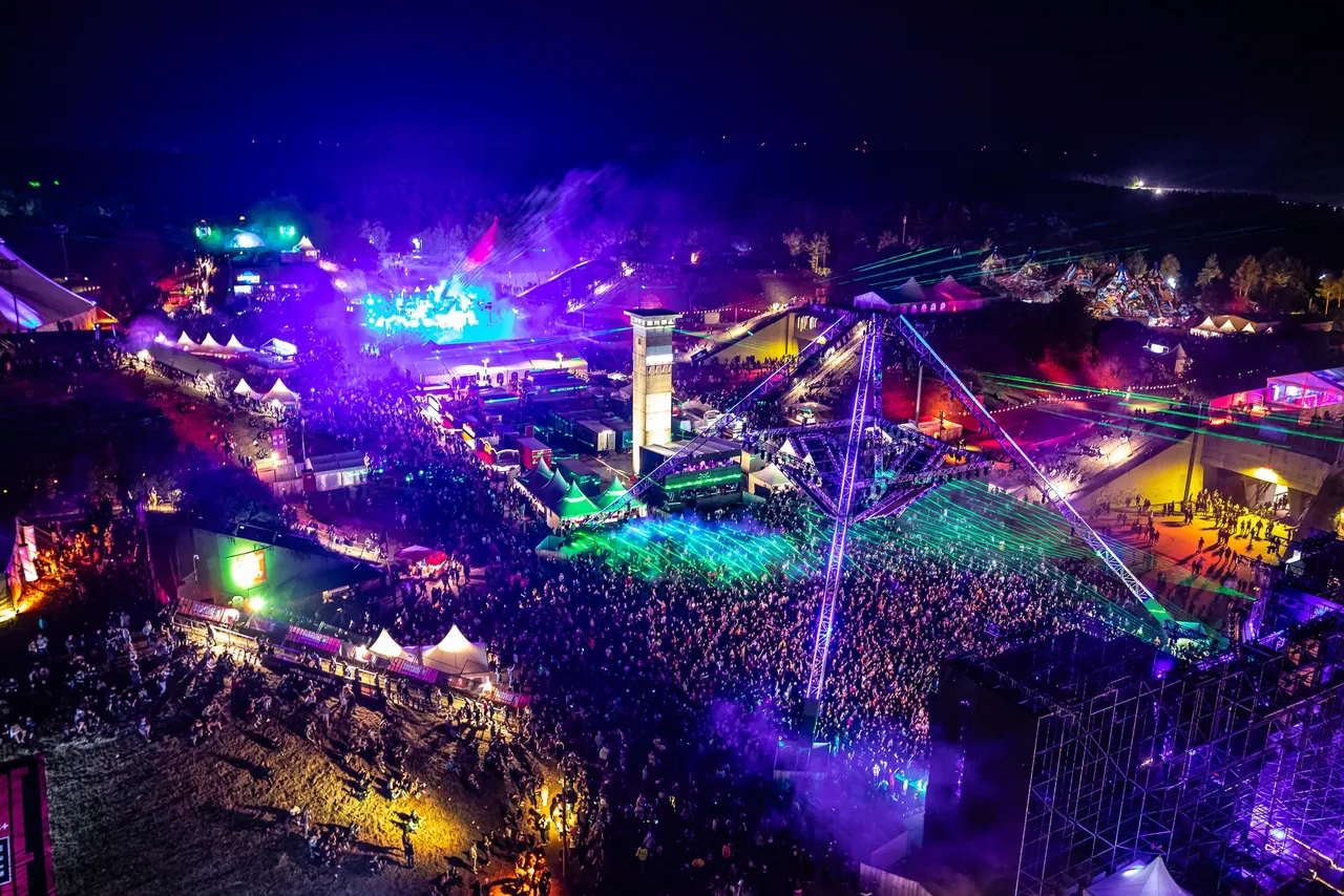 Vue en hauteur de la Pydna de nuit en 2023 : la foule de l'OpenAirFloor sous la structure en pyramide, la tour et les lasers.