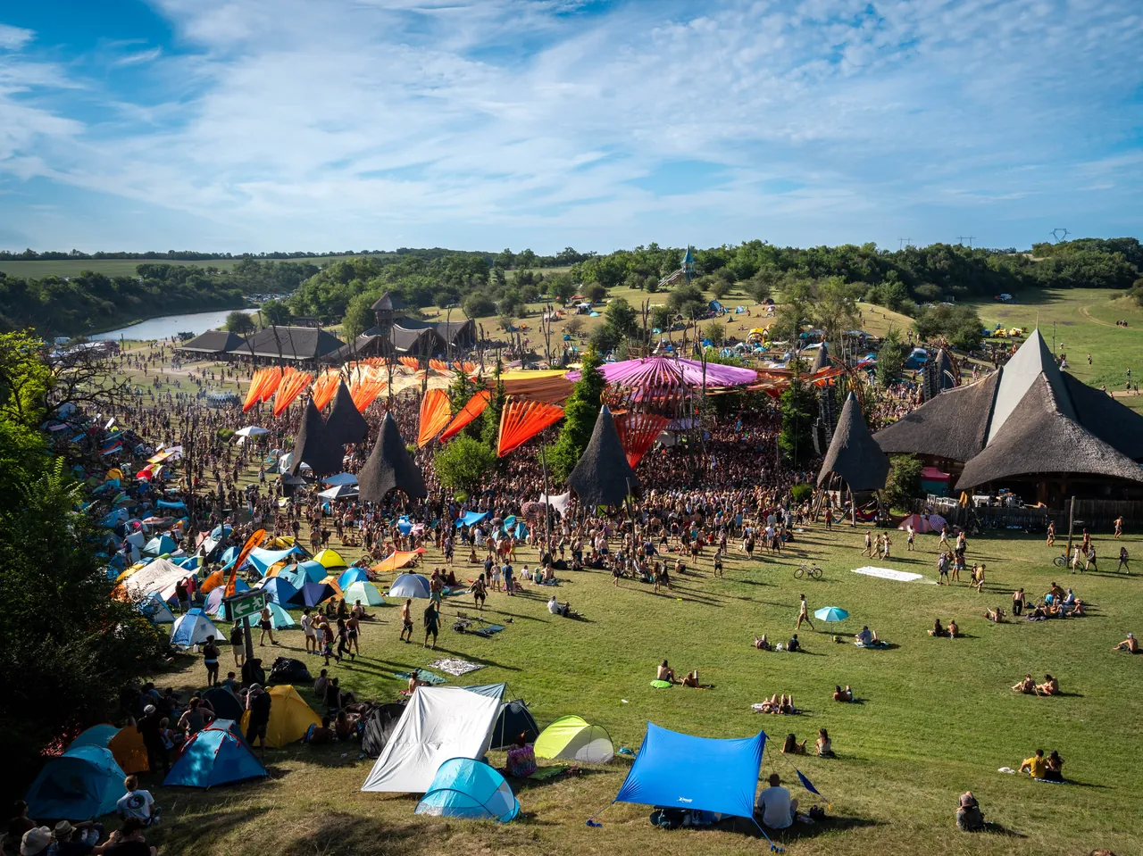 View from the hill over the Ozora Stage and its orange sails, the tipis, the campsites and the Dádpuszta lake, in August 2023.