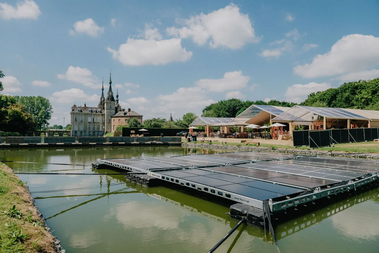 Le champ de panneaux solaires flottants sur l'étang, le château de Ribaucourt et les tentes du site derrière.