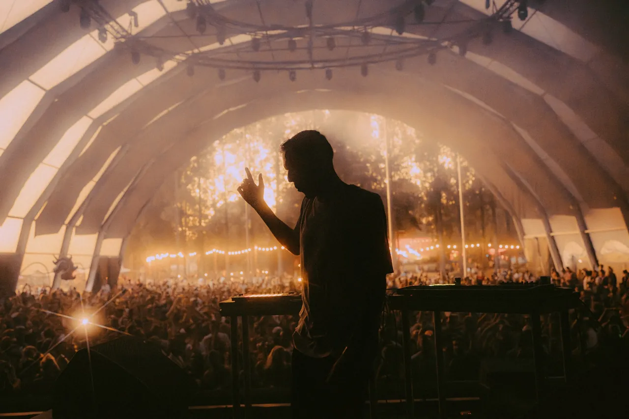 Un DJ en silhouette sous une scène couverte en forme de dôme, face à la foule, lors de l'édition 2025.