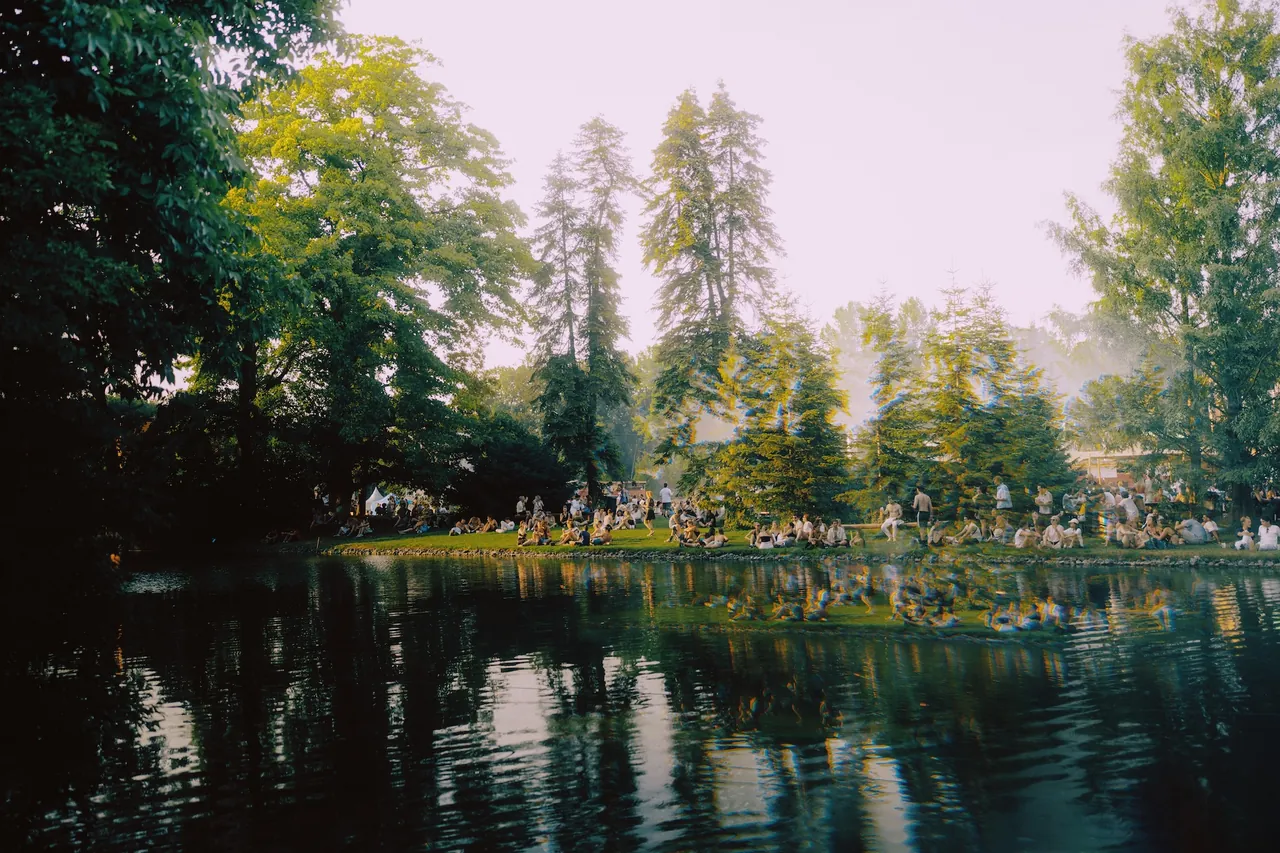 Le lac du domaine et, sur la rive opposée, les festivaliers sous les arbres, en 2026.