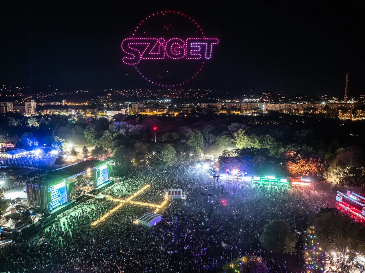 Spectacle de drones dessinant le logo Sziget au-dessus de l'île et de la Main Stage, le 11 août 2026 ; au fond, les immeubles d'Óbuda.
