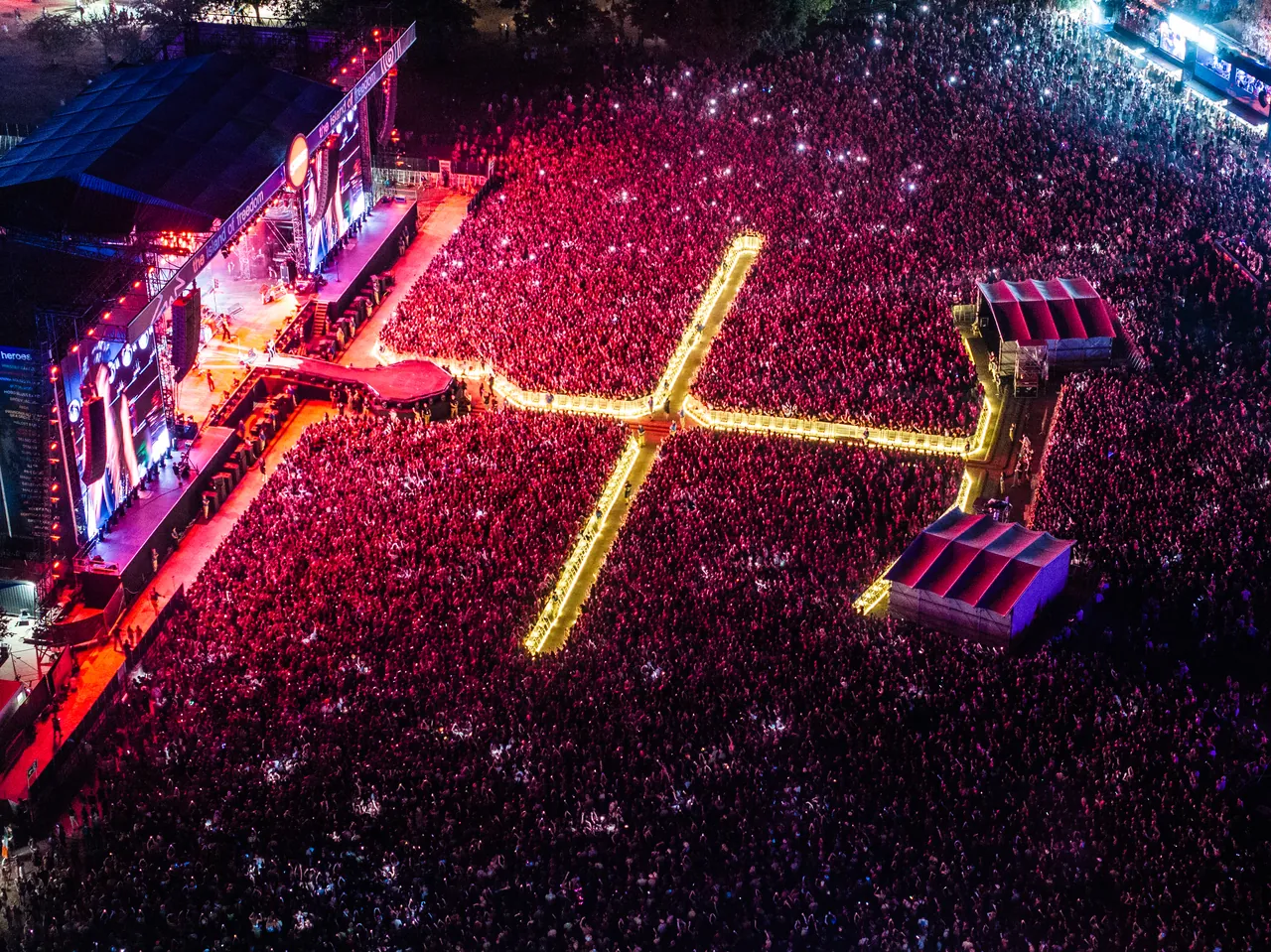Vue aérienne de la Main Stage et de sa passerelle en croix éclairée au milieu du public, le 11 août 2026, premier soir du programme principal.