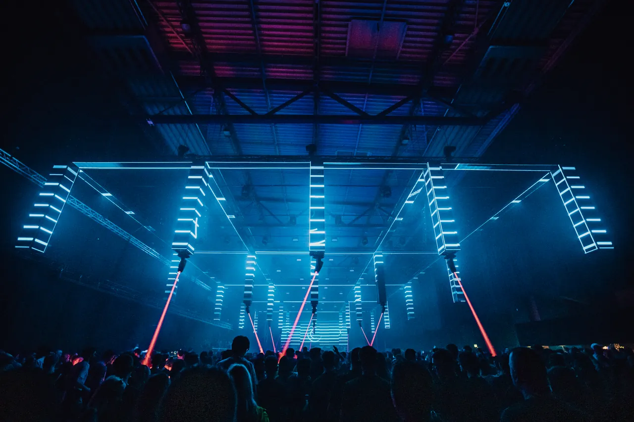 Une structure de LED suspendue sous la charpente de la Maimarkthalle, percée de lasers rouges, édition d'avril 2019 (25 ans).