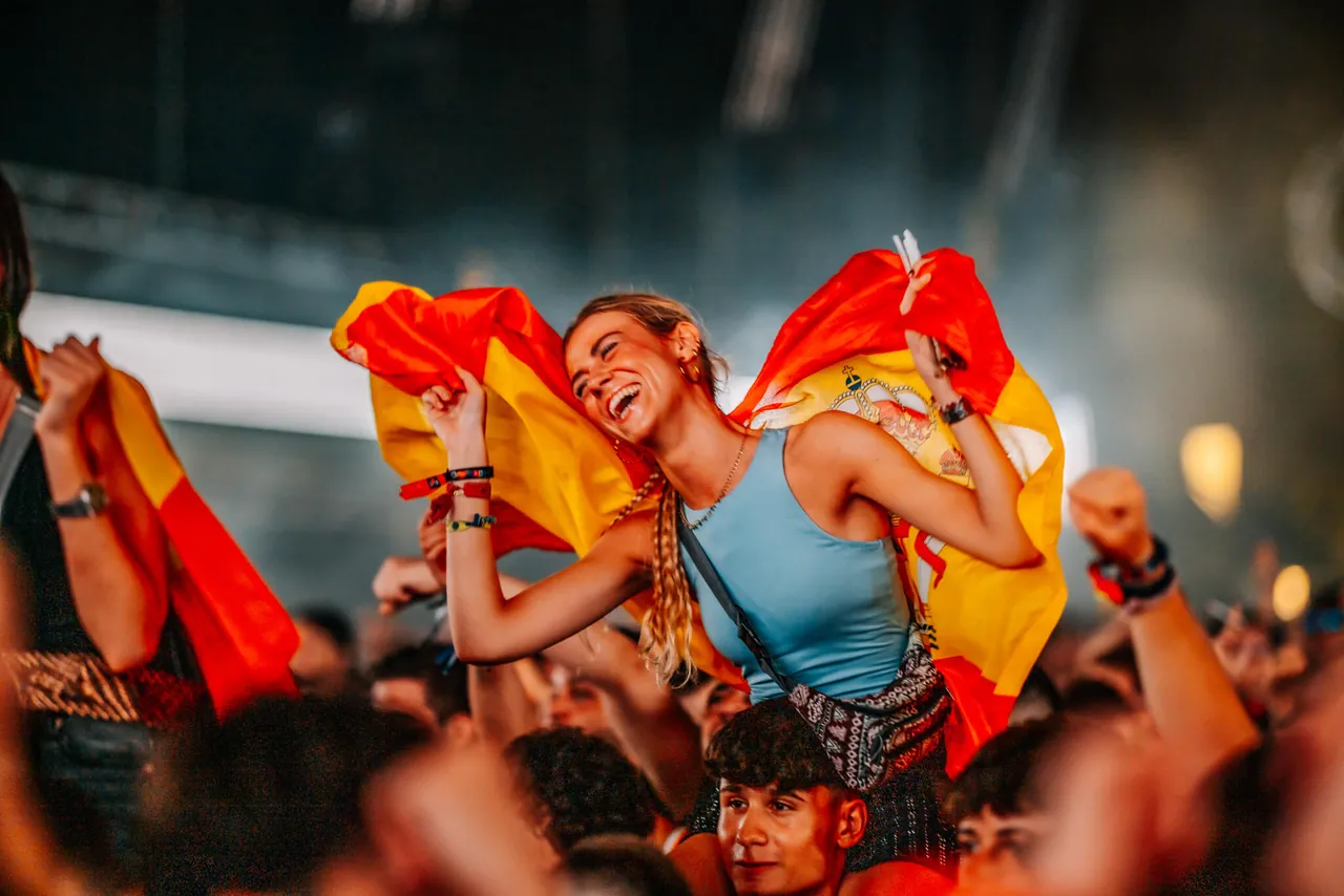 Une festivalière juchée sur des épaules, drapeau espagnol sur le dos, en 2024.