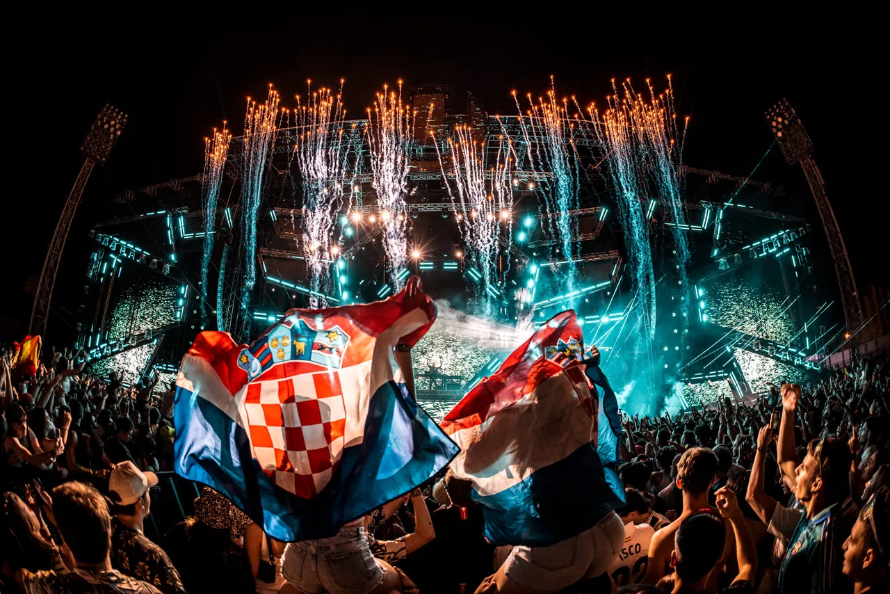 Drapeaux croates brandis face au Mainstage pendant un tir pyrotechnique, en 2025.