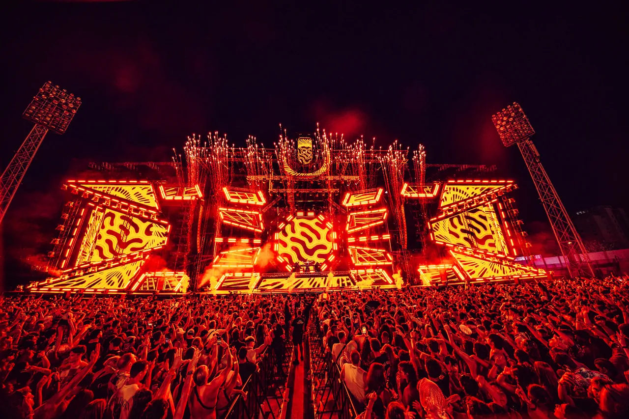 Le Mainstage de 2025 embrasé d'orange, pyrotechnie au sommet, entre deux pylônes d'éclairage.