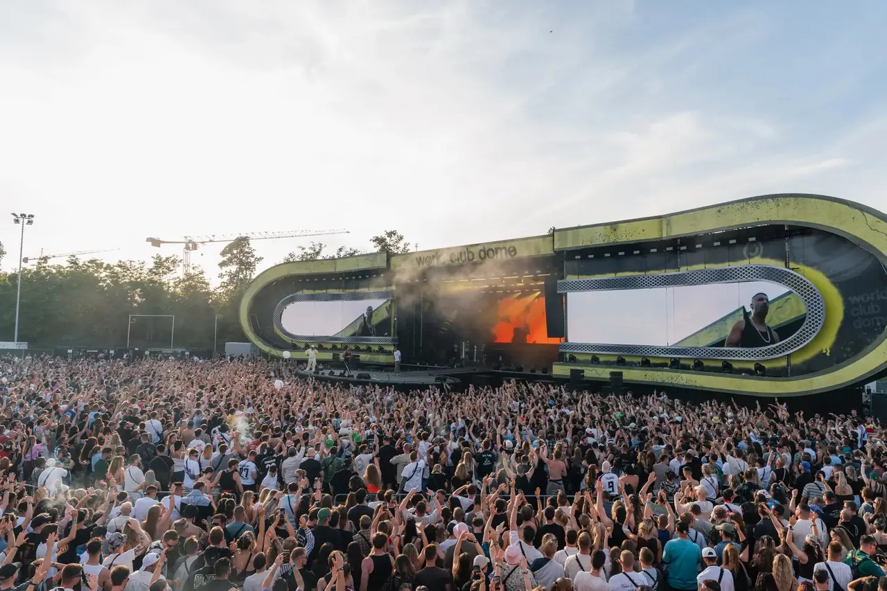 The large ring-shaped outdoor stage in front of a packed daytime crowd.