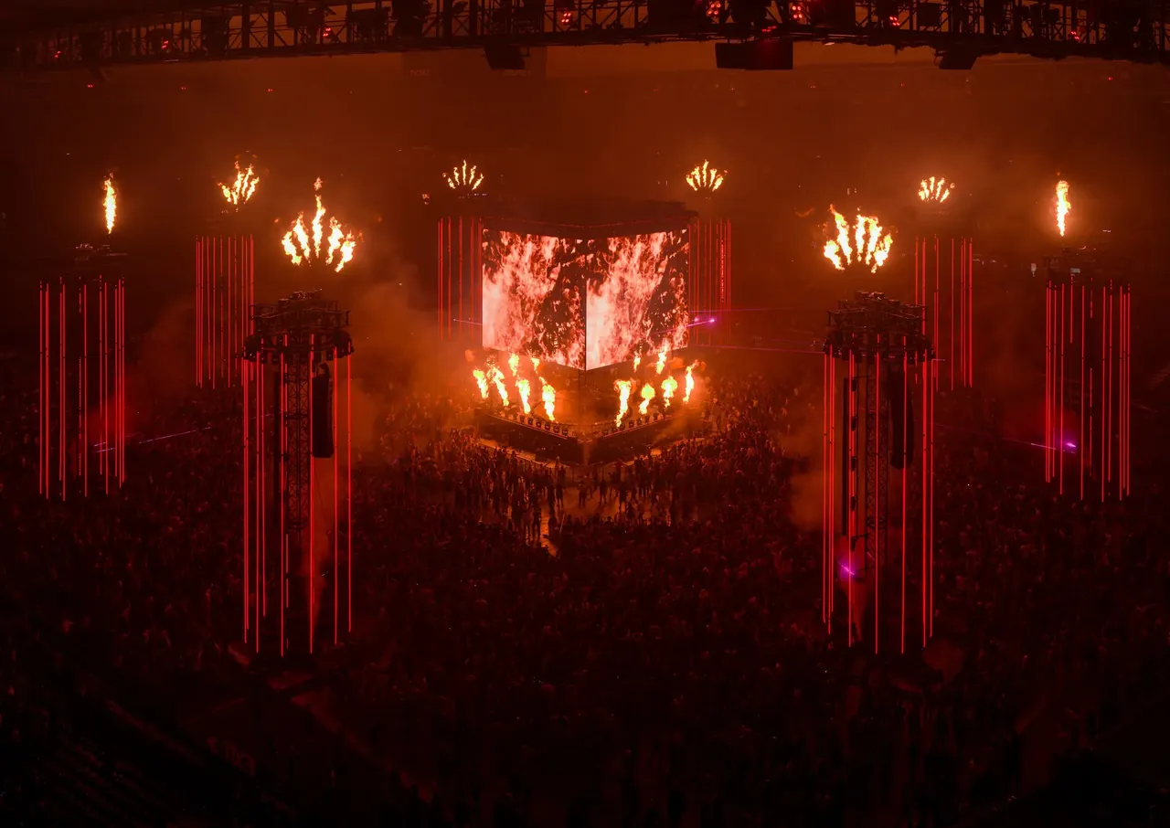 The 360-degree centre stage in the middle of the stadium pitch at night, between its flame towers.