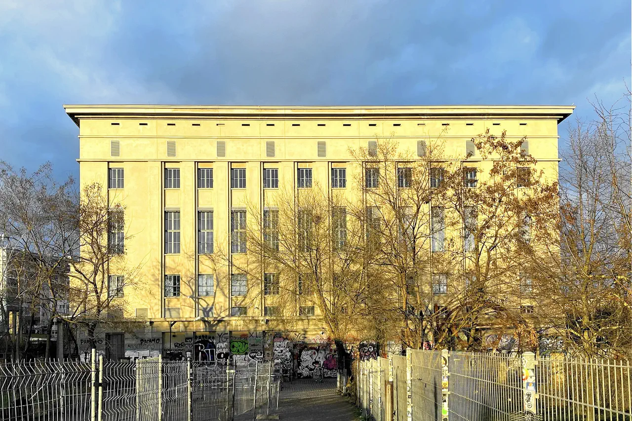 Façade du Berghain, ancienne centrale électrique de Berlin, éclairée par le soleil derrière des arbres sans feuilles et une clôture métallique