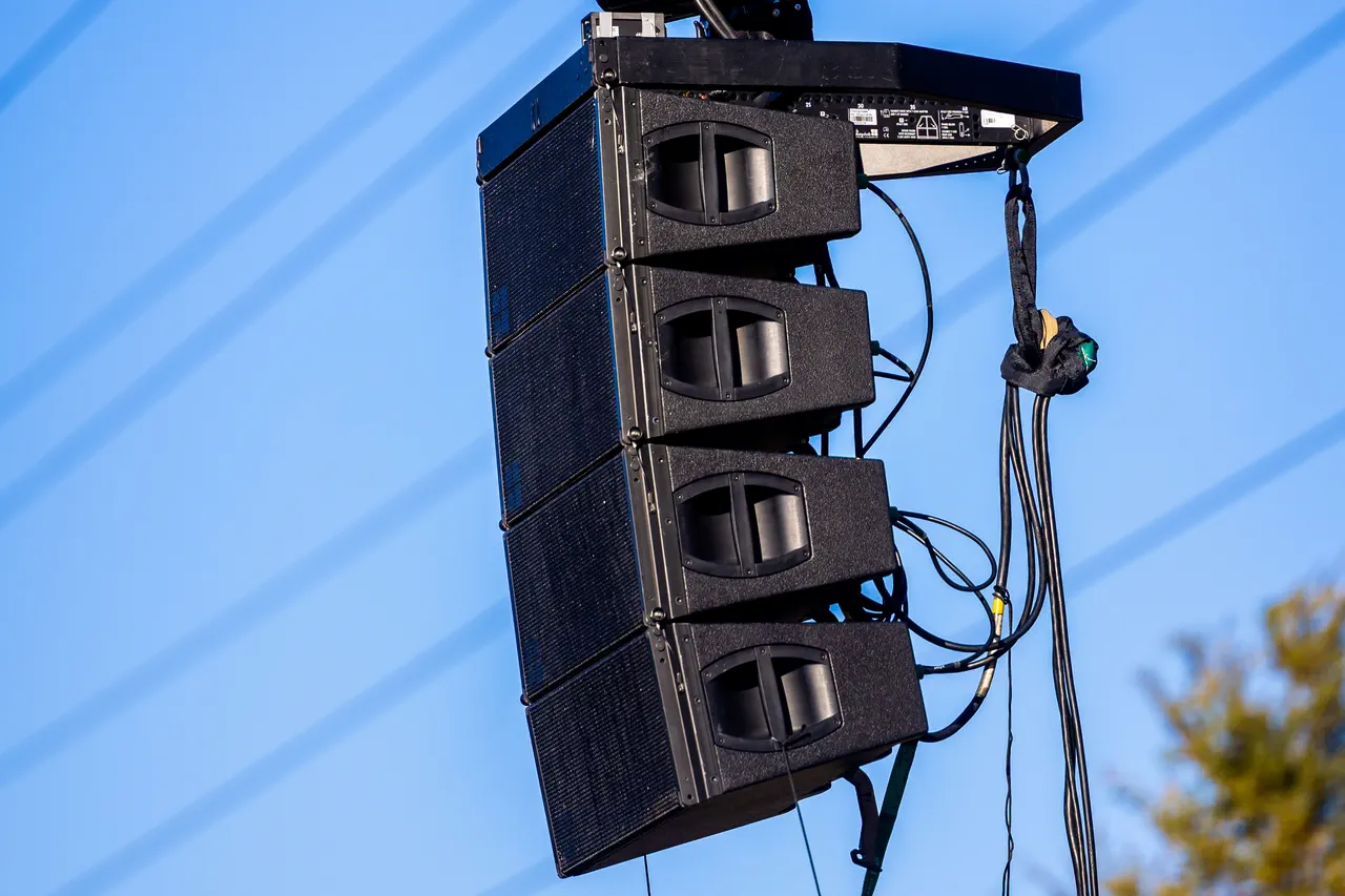 Grappe d’enceintes line array suspendue en plein air, avec ses câbles, sur fond de ciel bleu